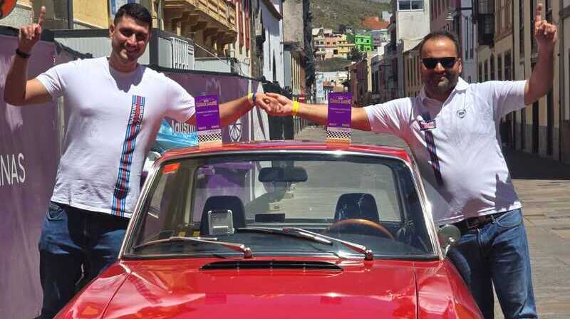foto de los ganadores. posan de pie a ambos lados de su lancia fulvia rojo. los trofeos encima del techo del coche