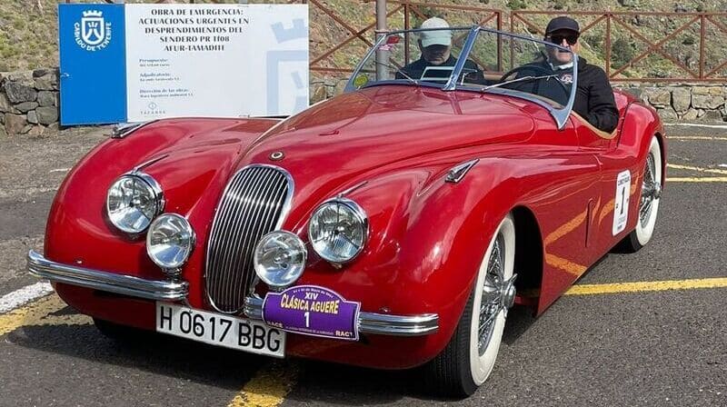 foto de jaguar xk 120 ots rojo con piloto y navegante dentro. Al fondo paisaje montañoso